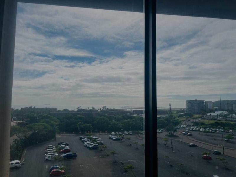 An elevated view from an interior space looking out over a large parking area and coastal landscape.