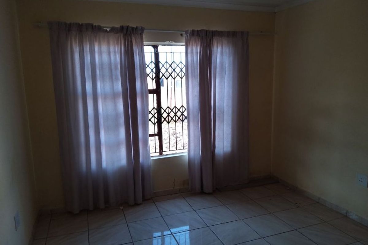 An empty bedroom featuring tiled flooring and a window fitted with a security gate.