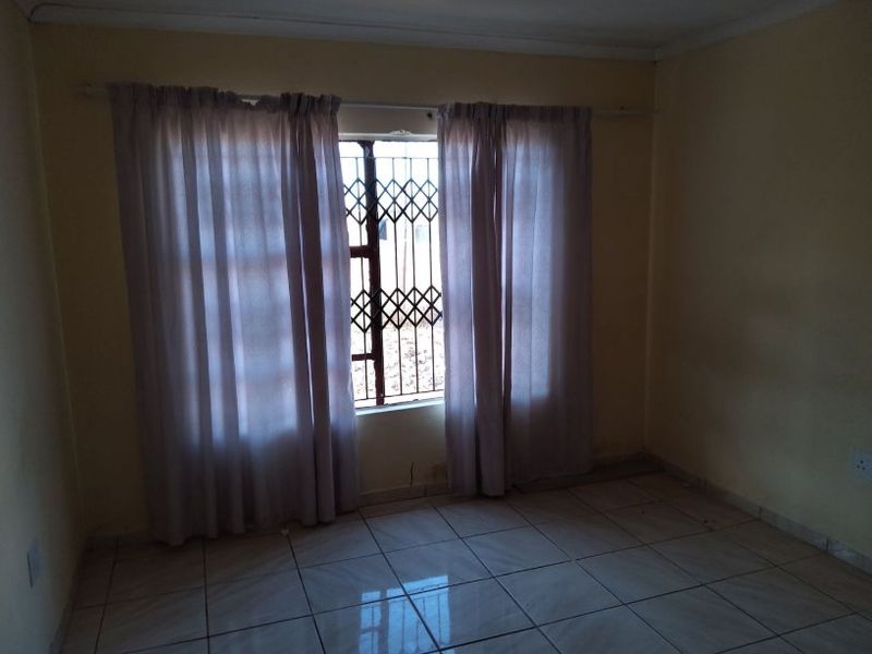 An empty bedroom featuring tiled flooring and a window fitted with a security gate.