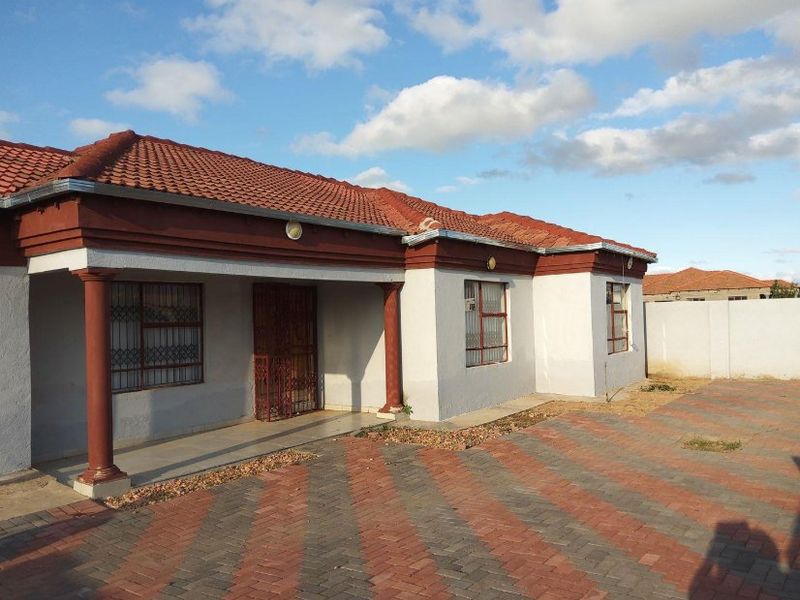 Front view of a single-story house featuring a tiled roof, covered porch with decorative columns, security gates, and a paved driveway.
