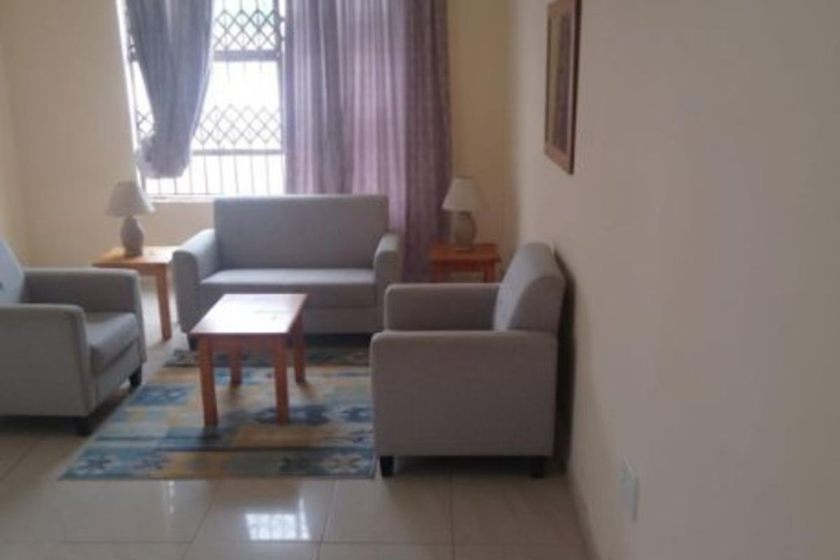 A living room featuring tiled flooring and a window with security bars, showing visible signs of wall surface damage and peeling paint.