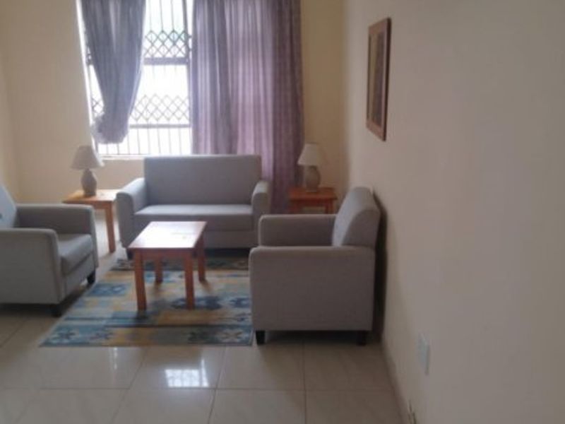 A living room featuring tiled flooring and a window with security bars, showing visible signs of wall surface damage and peeling paint.
