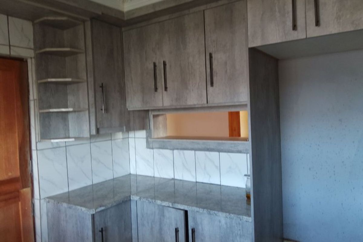 A kitchen area featuring grey laminated cabinetry, granite countertops, and a marble-look tiled backsplash with a convenient pass-through window to the adjacent room.