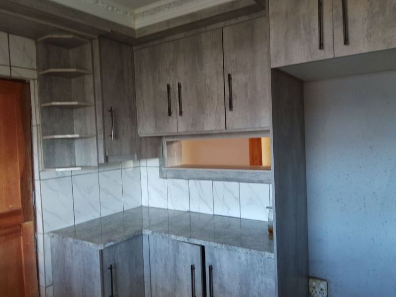 A kitchen area featuring grey laminated cabinetry, granite countertops, and a marble-look tiled backsplash with a convenient pass-through window to the adjacent room.
