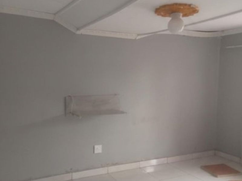 An empty bedroom featuring tiled flooring, a ceiling rose, and a wall-mounted shelf, requiring cosmetic updates to improve its overall appeal.