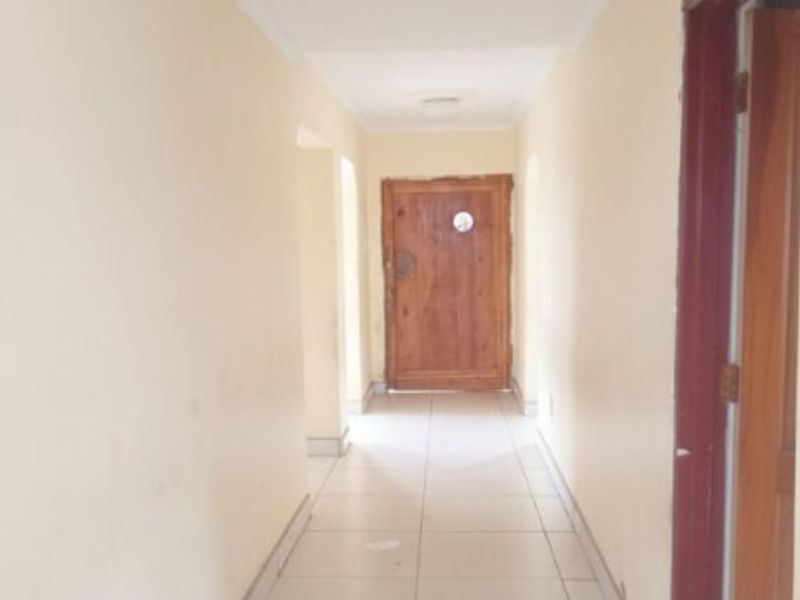 A vacant interior hallway featuring tiled flooring, a ceiling rose, and a wooden door, showing signs of wear on the walls and door frame.