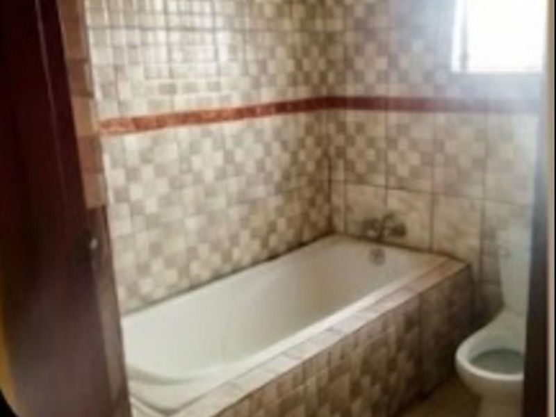 A functional bathroom featuring a built-in bathtub with tiled surround and a standard toilet, offering a dated but practical layout.