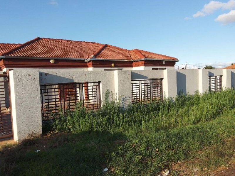Front view of a single-story house featuring a tiled roof and a perimeter wall with integrated metal security gates.