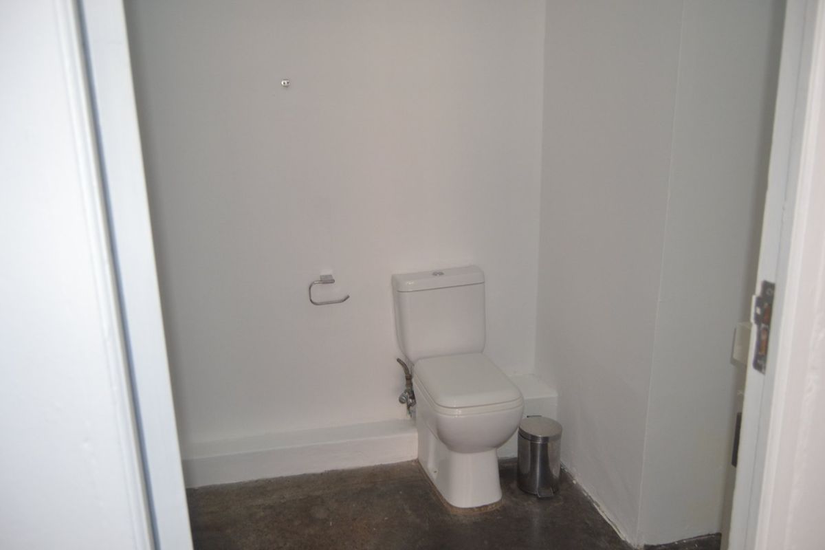 A compact, minimalist bathroom featuring a white toilet and unfinished concrete flooring, offering a blank canvas for renovation and modern finishes.