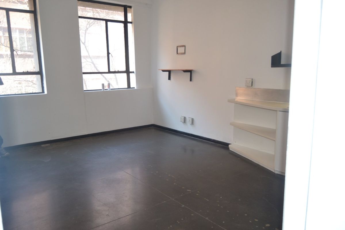 An empty living area featuring large windows, dark concrete flooring, and built-in shelving units, offering a blank canvas for interior design.