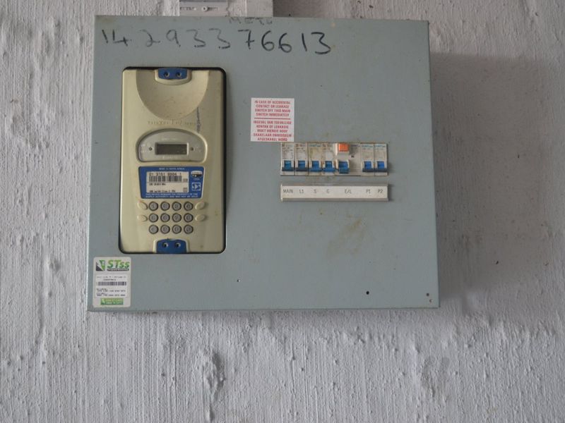 A wall-mounted prepaid electricity meter and electrical distribution board with circuit breakers.