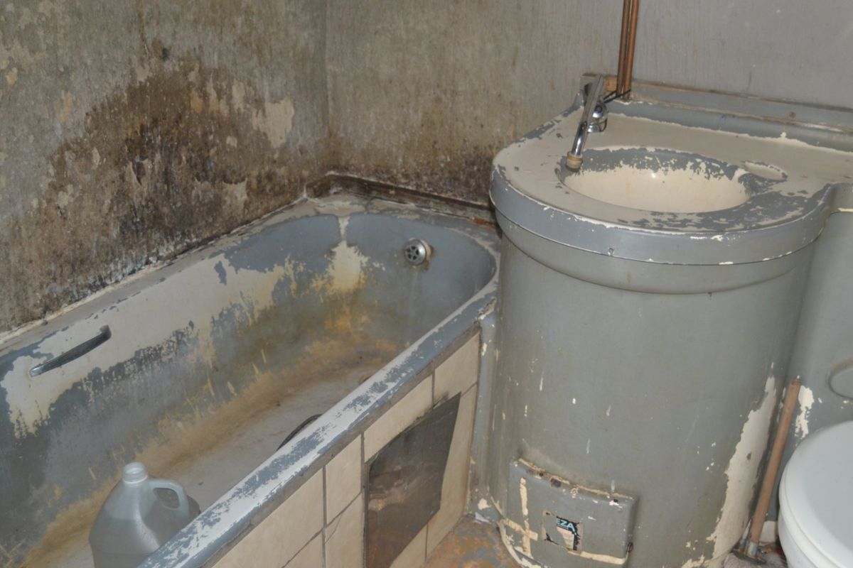 A bathroom in need of complete renovation, featuring a dated bathtub and pedestal basin with significant wear and surface damage.