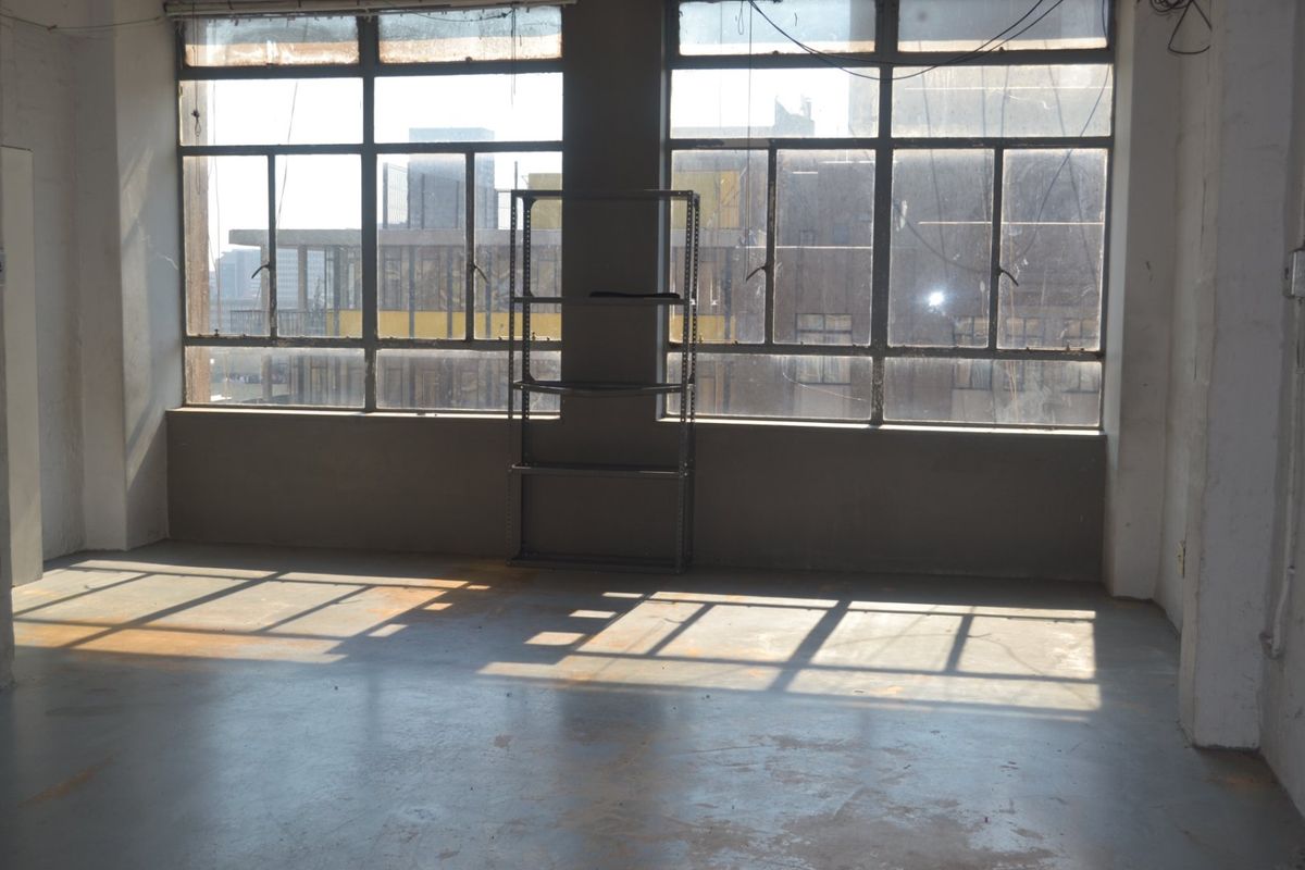 An empty industrial-style living space featuring large steel-framed windows and raw concrete flooring, offering a blank canvas for renovation.