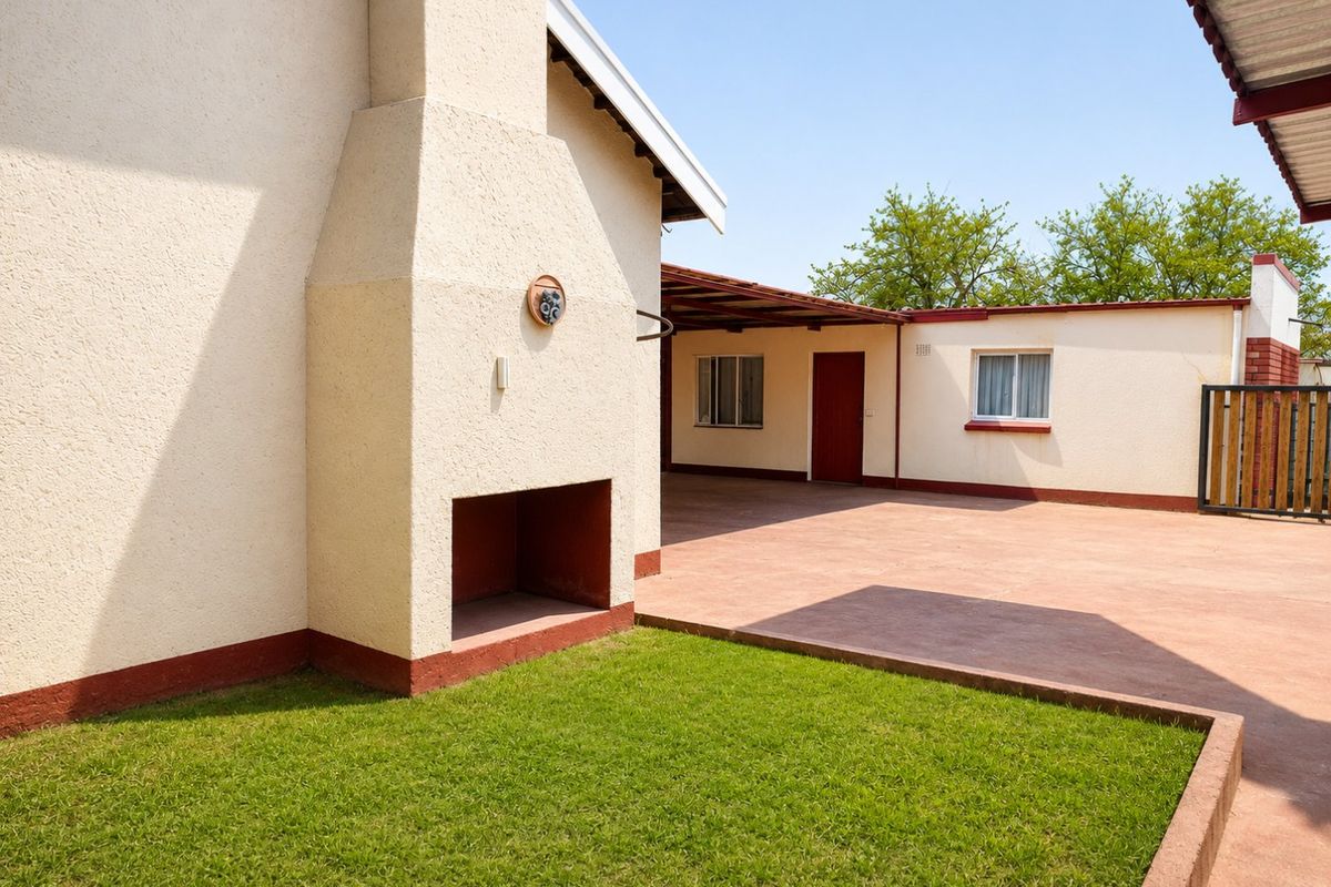 A well-maintained rear exterior area featuring a paved patio, a built-in outdoor fireplace, and a small lawn.