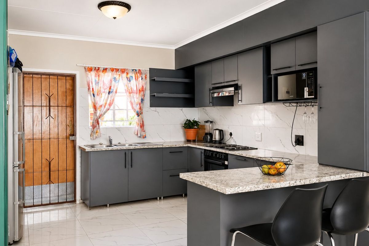 Modern kitchen featuring dark grey cabinetry, granite countertops, built-in appliances, marble-look splashback tiles, and tiled flooring with an adjacent security door.