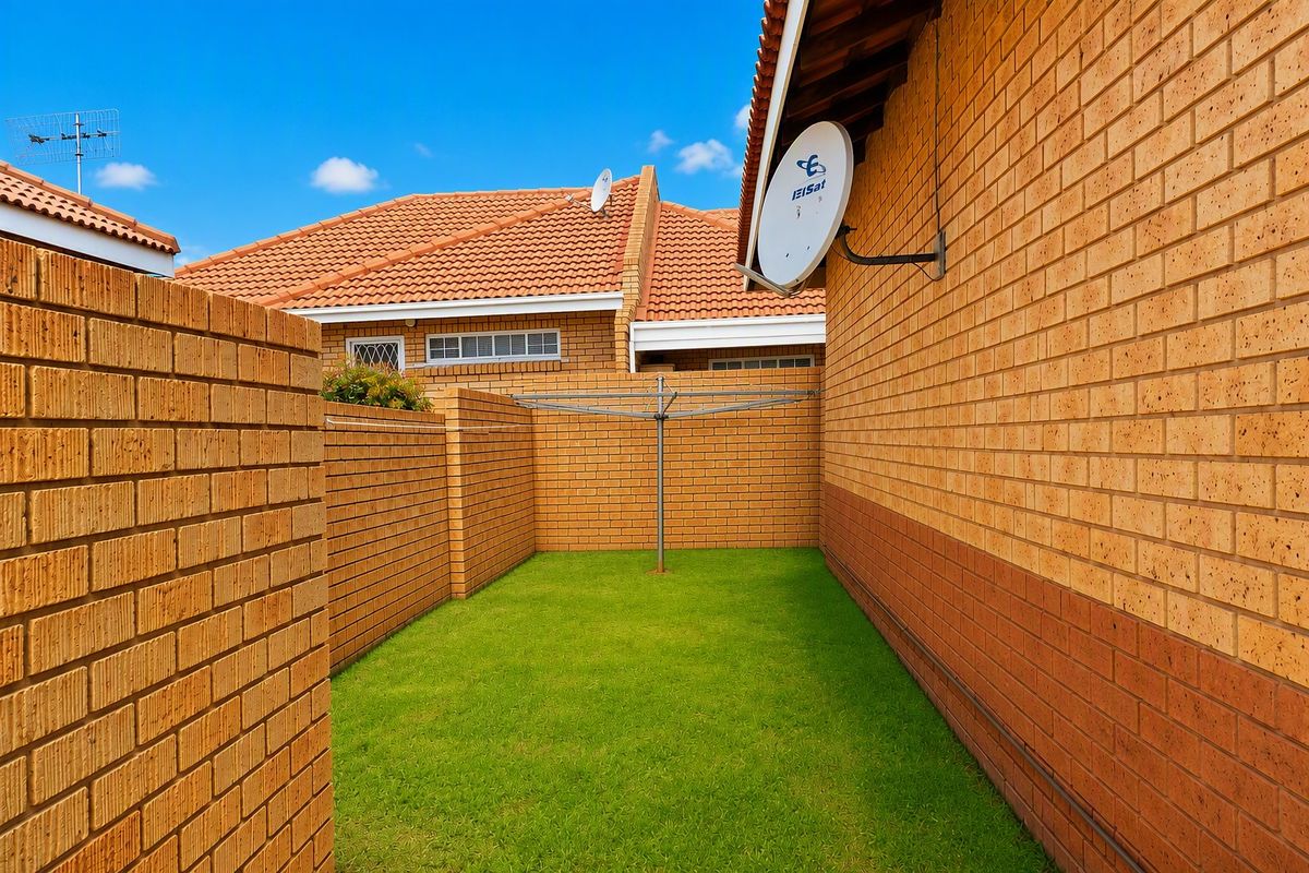 A private rear courtyard featuring brick boundary walls, a small lawn area, and a mounted satellite dish.