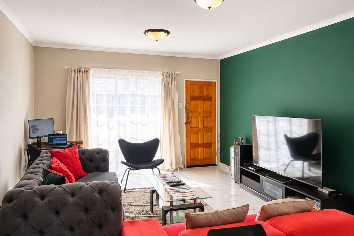 A well-lit living room featuring tiled flooring, a bold green accent wall, and a timber entrance door.