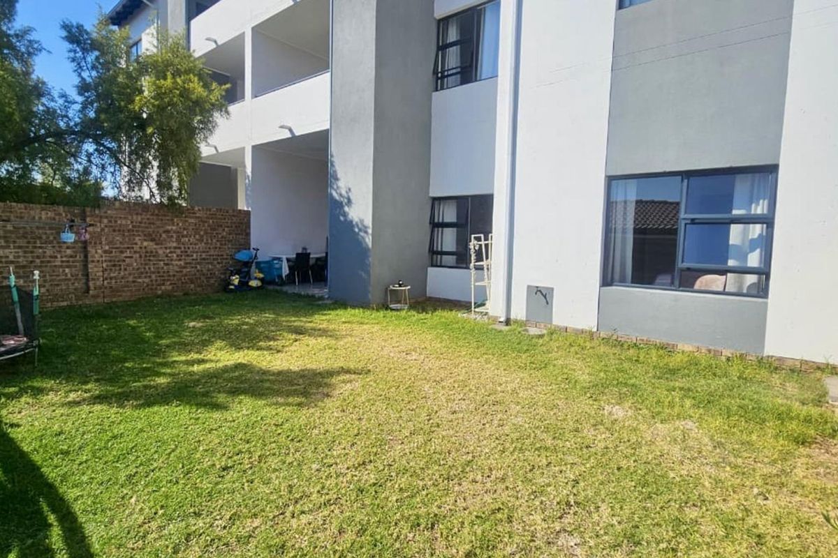 Rear view of the apartment building featuring a private garden area, brick boundary wall, timber fencing, and a covered patio space.