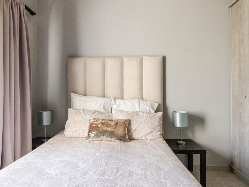 A well-maintained bedroom featuring neutral tones, a built-in wardrobe, tiled flooring, and a large window providing natural light.