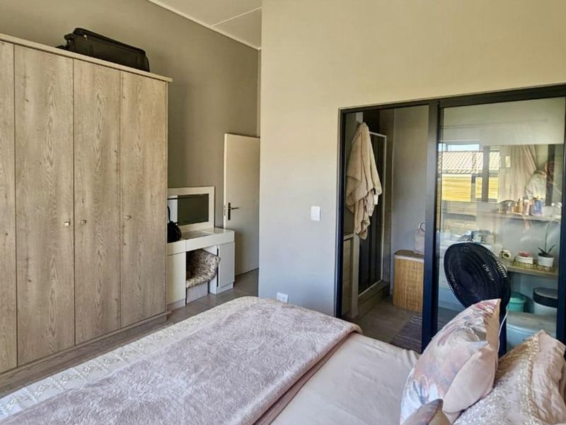 A well-maintained bedroom featuring a large built-in wardrobe and a modern glass partition wall providing a view into the en-suite bathroom.