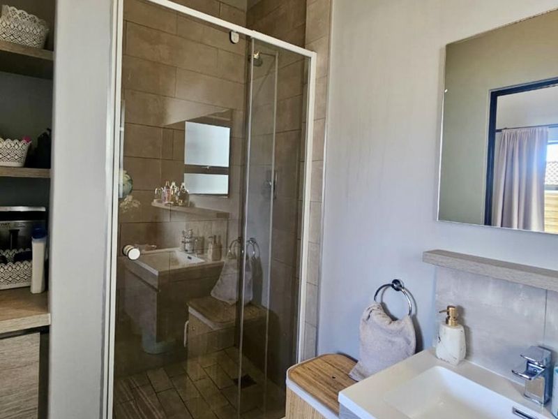 A modern bathroom featuring a glass-enclosed shower, vanity basin with mixer tap, wall-mounted mirror, and convenient built-in shelving for storage.