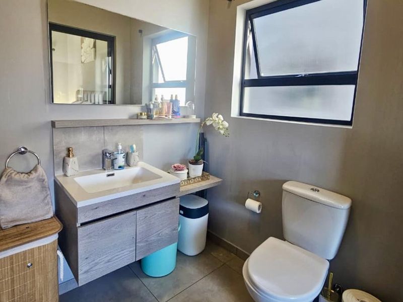 A functional bathroom featuring a modern vanity cabinet with a ceramic basin, wall-mounted mirror, and a standard toilet with tiled flooring.