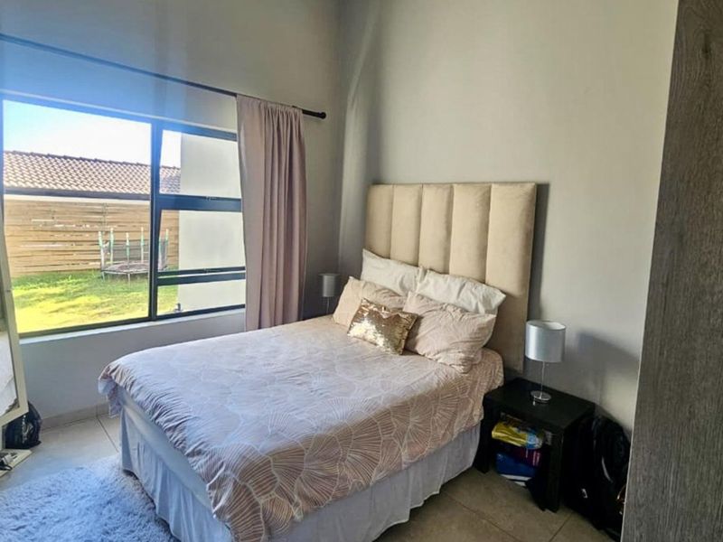 A well-lit bedroom featuring tiled flooring and a large window with views of the garden area.