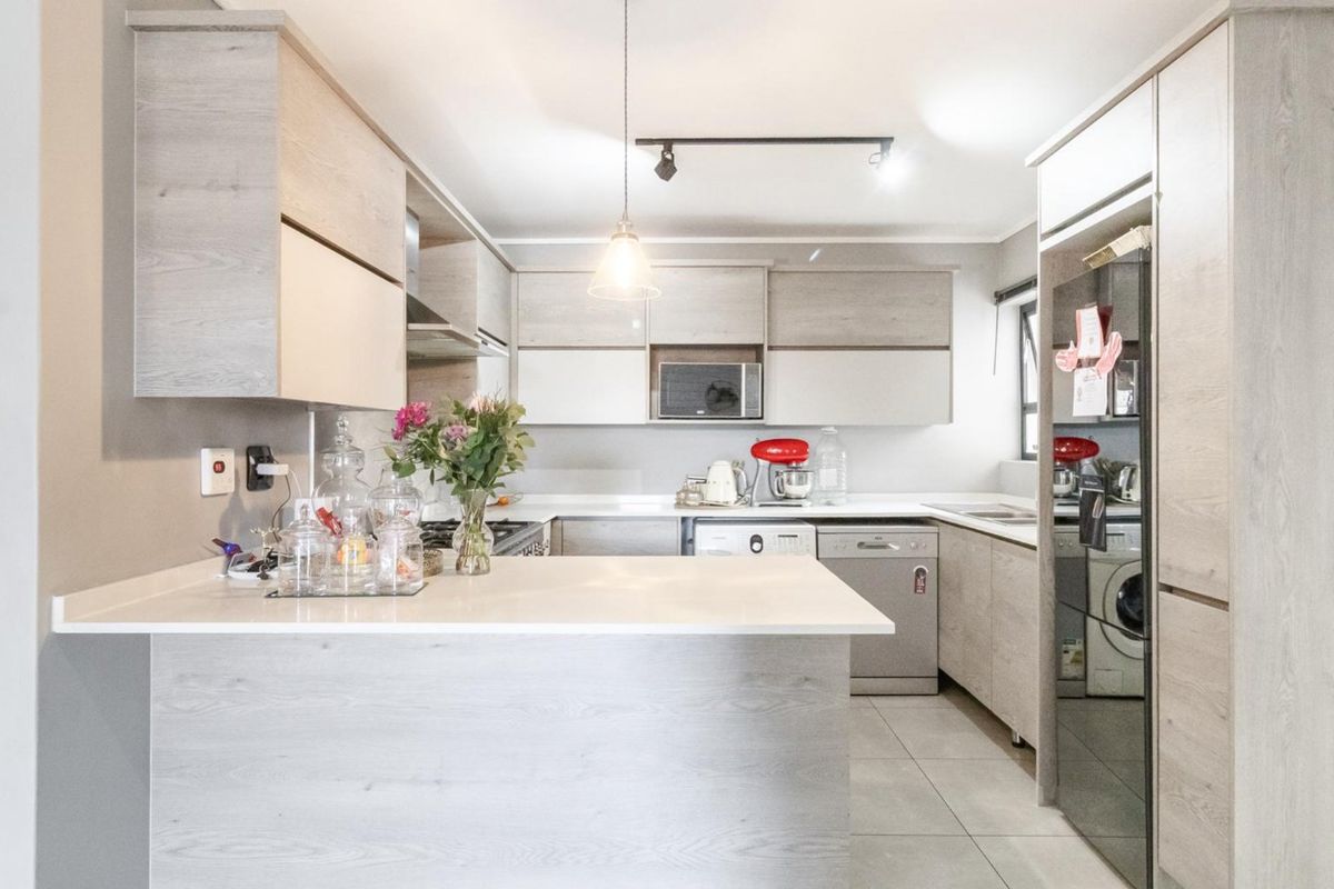 Modern kitchen featuring light wood-grain cabinetry, stone countertops, a breakfast bar, and integrated appliances, offering a clean and functional culinary space.