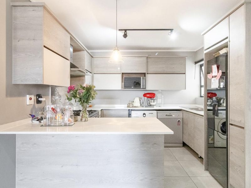 Modern kitchen featuring light wood-grain cabinetry, stone countertops, a breakfast bar, and integrated appliances, offering a clean and functional culinary space.