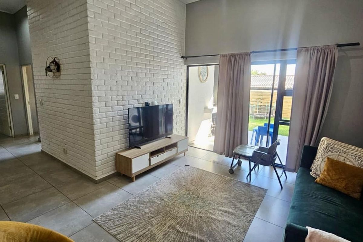 A bright living room featuring a white exposed brick accent wall, large format floor tiles, and sliding glass doors leading to an outdoor area.