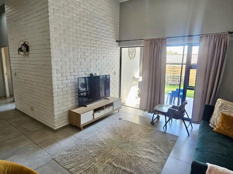 A bright living room featuring a white exposed brick accent wall, large format floor tiles, and sliding glass doors leading to an outdoor area.