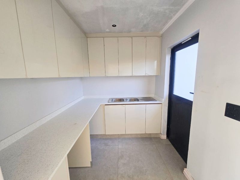 A functional scullery or laundry area featuring built-in cabinetry, a double sink, stone-look countertops, and direct access to the exterior.