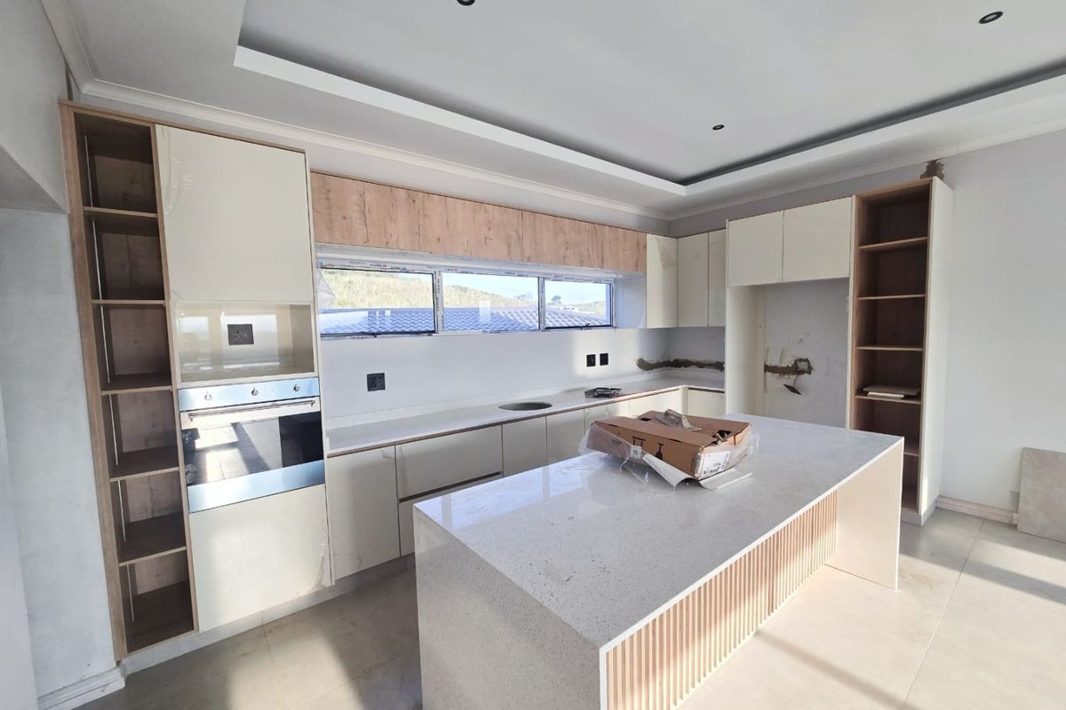 Modern kitchen featuring a central island, quartz countertops, and built-in oven, currently in an unfinished state with pending backsplash and electrical finishing.