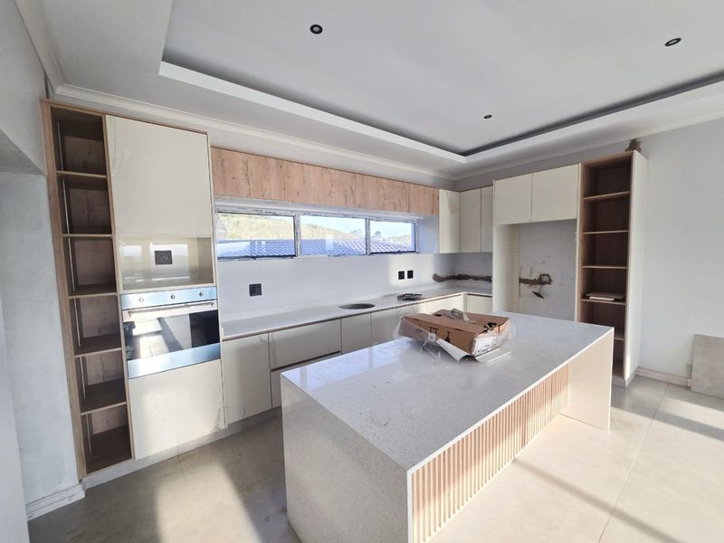 Modern kitchen featuring a central island, quartz countertops, and built-in oven, currently in an unfinished state with pending backsplash and electrical finishing.