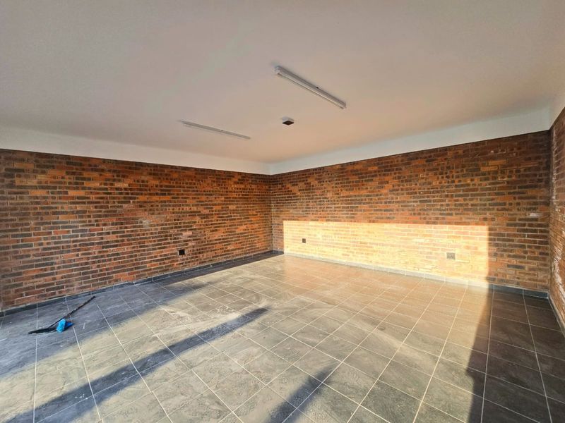An empty, open-plan living space featuring exposed brick walls and dark tiled flooring, offering a blank canvas for interior design.