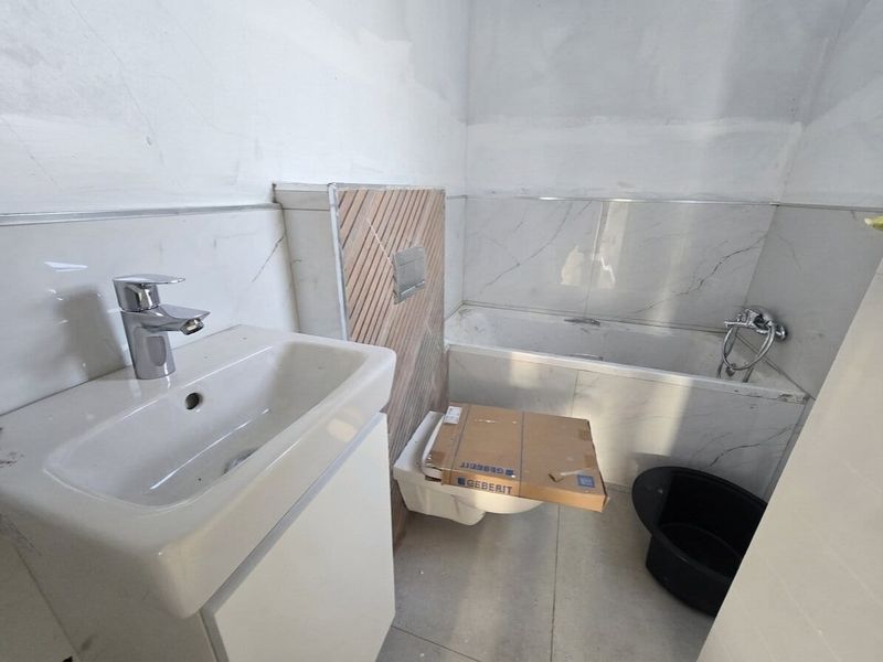 A bathroom under construction featuring a wall-mounted vanity, built-in bathtub, and wall-mounted toilet with marble-effect tiling and unfinished wall surfaces.