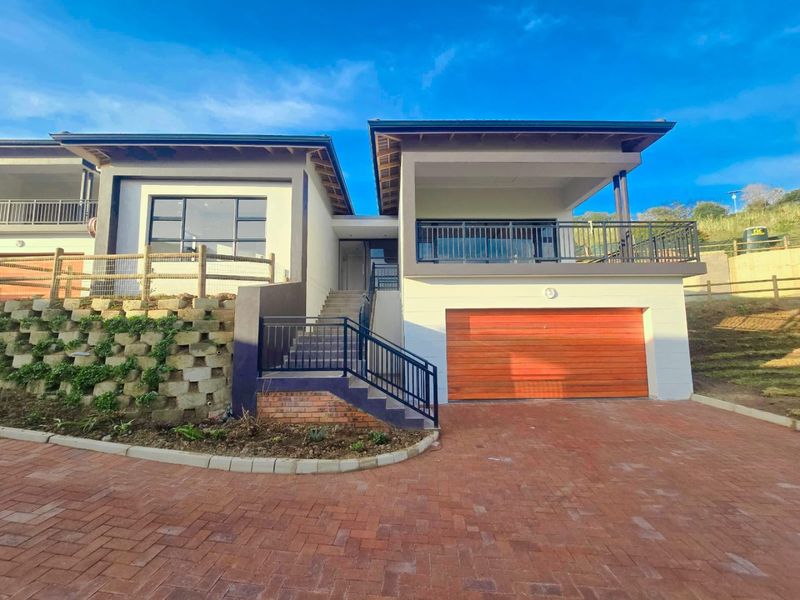Modern double-story house exterior featuring a paved driveway, timber garage door, and an elevated balcony with metal railings.