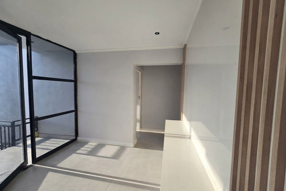 Modern, bright living area featuring sleek black steel-framed glass doors, timber slat wall detailing, and clean tiled flooring.