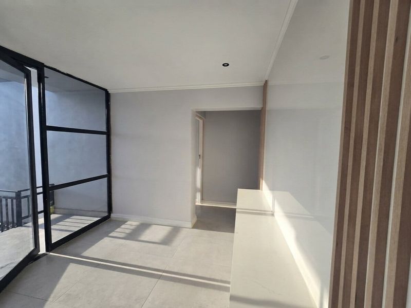 Modern, bright living area featuring sleek black steel-framed glass doors, timber slat wall detailing, and clean tiled flooring.