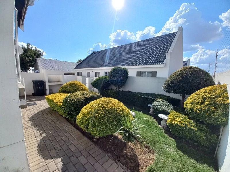 A well-maintained rear garden featuring a paved patio area, built-in braai, and manicured landscaping with a secure boundary wall.