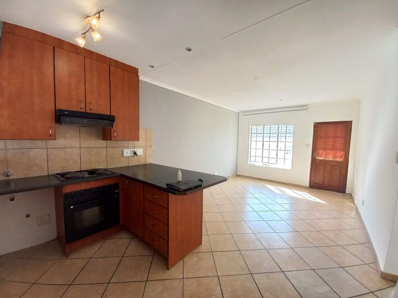 Open-plan kitchen and living area featuring wooden cabinetry, built-in appliances, tiled flooring, and direct access to the exterior via a timber door.