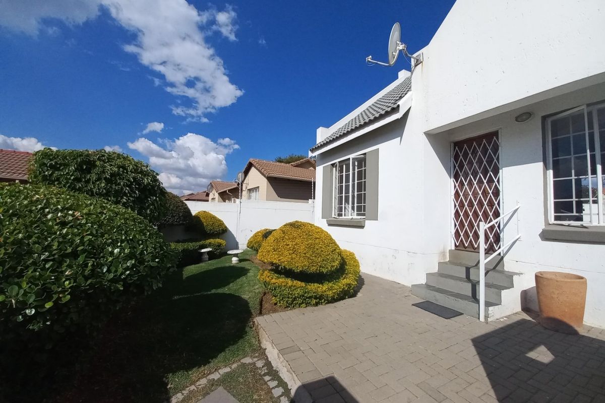 A well-maintained rear exterior view of the townhouse featuring a paved patio area, landscaped garden, and secure entrance with a metal security gate.