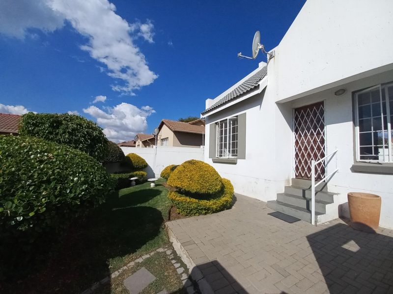 A well-maintained rear exterior view of the townhouse featuring a paved patio area, landscaped garden, and secure entrance with a metal security gate.