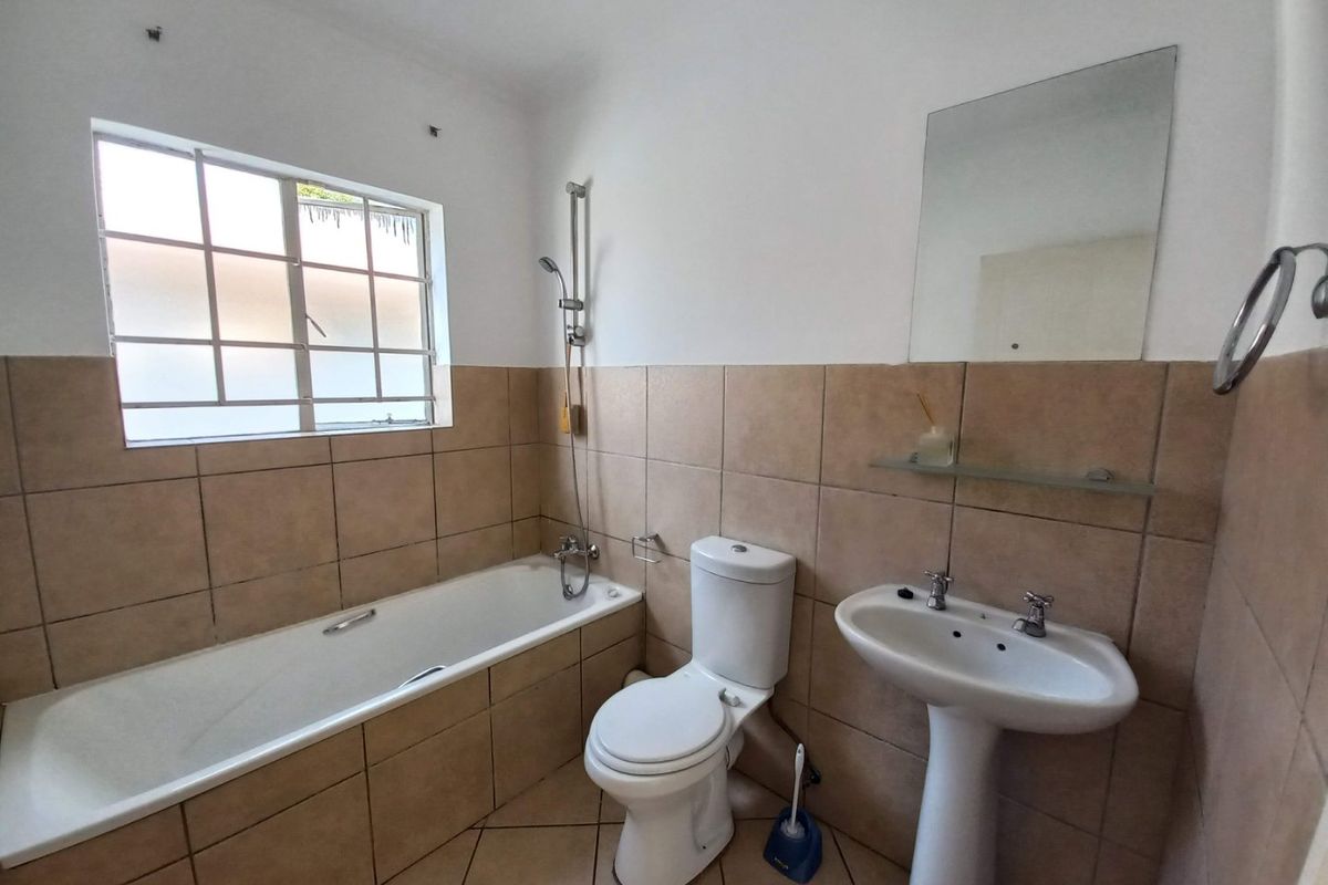 A functional bathroom featuring a bathtub with shower mixer, pedestal basin, toilet, and neutral wall tiling.