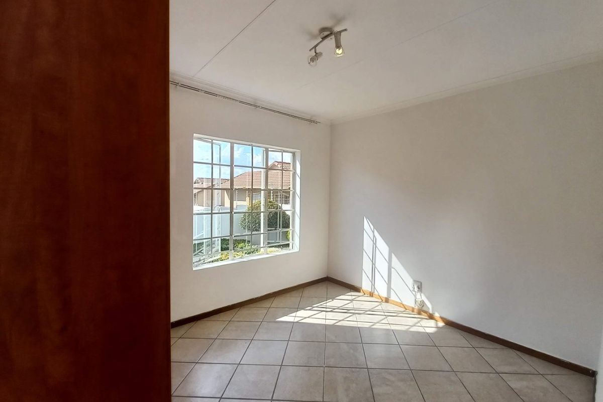 A bright, empty bedroom featuring neutral tiled flooring, a grid-pattern window, and a ceiling-mounted spotlight fixture.