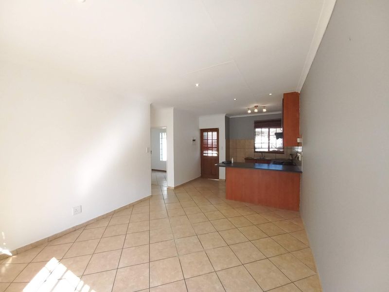 An open-plan living and kitchen area featuring tiled flooring, built-in cabinetry, and a breakfast bar, offering a functional and versatile layout.