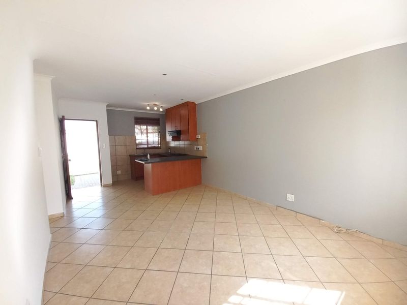Open-plan living area featuring tiled flooring and a functional kitchen with built-in cabinetry, extractor fan, and direct access to the exterior.