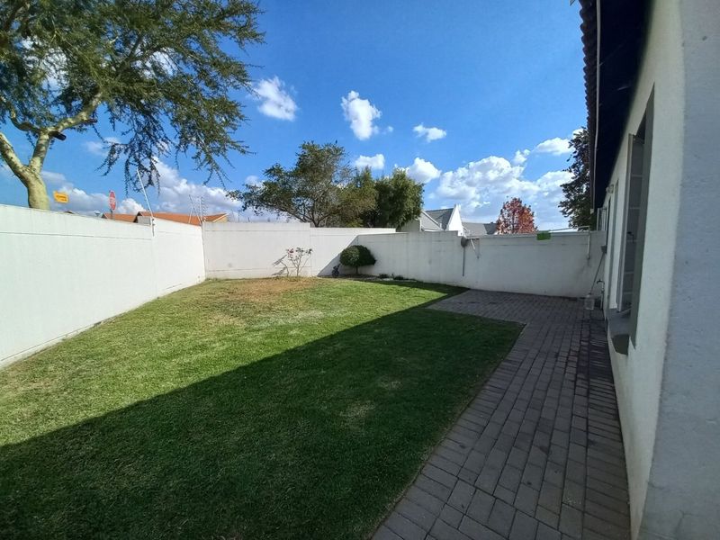 A private rear garden featuring a paved walkway, lawn area, and high perimeter boundary walls, offering a secure outdoor space.