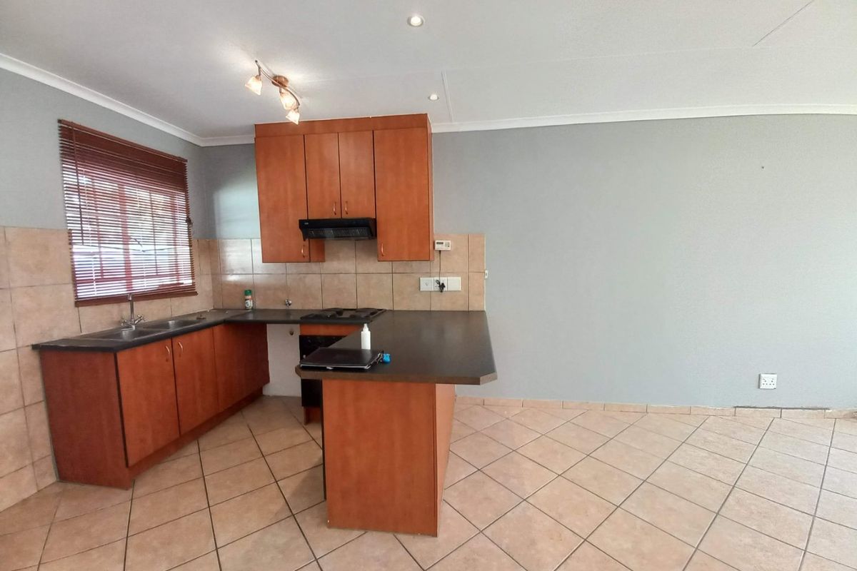 A functional kitchen featuring wooden cabinetry, laminate countertops, a built-in hob with extractor fan, and tiled flooring in an open-plan layout.