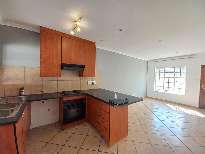 Open-plan kitchen and living area featuring wooden cabinetry, built-in oven, hob, and tiled flooring, offering a functional layout ready for modern updates.